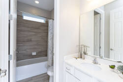 Welcome to this inviting bathroom, where natural light pours in through a frosted window, accentuating the warm wood paneling and sleek white cabinetry. The modern fixtures and clean lines make it an ideal space for relaxation.
