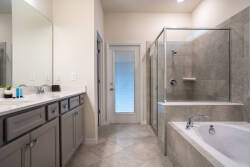This bright bathroom features sleek gray tiles and a spacious glass-enclosed shower, offering a modern touch. With dual sinks and a large mirror, it enhances the airy feel, making it perfect for your morning routine.