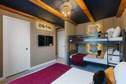 This cozy room features a stylish bunk bed with maroon accents, warm wooden beams, and soft lighting for a welcoming atmosphere. A sleek wall-mounted TV adds modern convenience for relaxing after a day of adventure.