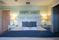 Welcome to this beautifully decorated bedroom with a plush king-sized bed dressed in crisp white linens and cozy navy accents, where soft ambient lighting from stylish bedside lamps sets a tranquil atmosphere for your relaxation.