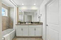 Enjoy the bright bathroom with sleek white cabinetry and a chic gray countertop, offering plenty of space for your essentials. A large mirror reflects natural light from the window, creating an airy and inviting atmosphere.