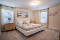 Welcome to this cozy bedroom with soft beige walls and plush gray carpeting, creating a warm atmosphere. The chic bed frame and sleek wood nightstands complement each other, while natural light enhances the calm vibe through.
