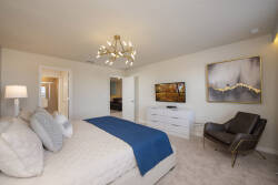This stylish bedroom offers a cozy king-size bed with crisp linens, a warm light carpet, and a striking chandelier. A sleek dresser and a comfy accent chair create an inviting space, ideal for relaxing after your adventures.
