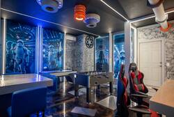 Have fun in a sci-fi space-themed game room with foosball, gaming chairs, a table for games or snacks, bold wall art, and blue LED lighting, creating an exciting spot for all ages.