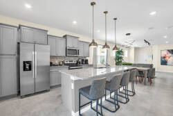 This bright and spacious kitchen boasts sleek gray cabinetry and a stunning quartz island ideal for casual dining. Modern pendant lights add elegance, while large windows bring in natural light, enhancing the inviting open layout.
