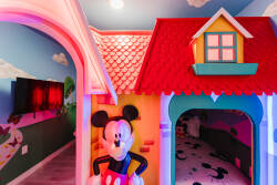 Welcome to a whimsical world for young adventurers, where a vibrant playhouse with a charming red roof and cheerful Mickey Mouse decor awaits. Bright colors and imaginative murals spark creativity in this joyful atmosphere.