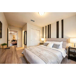 Rest in a warm bedroom with a cozy white bed, striped accent wall, soft lamps, beige curtains, neutral carpet, and calming decor for vacation comfort.