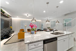 Welcome to a bright living space where sleek white cabinetry contrasts with a striking black wall. The spacious kitchen island, decorated with fresh flowers, invites you to enjoy casual dining under the warm glow of pendant.