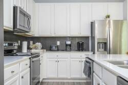 Welcome to a bright kitchen with crisp white cabinetry and sleek stainless-steel appliances, inspiring your culinary creativity. The modern gray backsplash enhances the ample counter space, ideal for all your cooking needs.