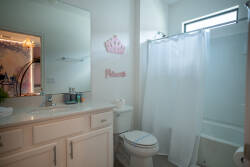 This bright bathroom features a sleek white vanity with ample counter space and a stylish mirror that enhances the natural light, while the light tiles and simple shower curtain create a refreshing start to your day.