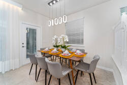 The dining area boasts a stylish wooden table for six with sleek gray chairs, complemented by a modern light fixture that casts a warm glow and large windows that fill the space with natural light for an inviting atmosphere.