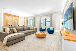 Enjoy the cheerful atmosphere of this bright living room, where a spacious gray sectional and vibrant blue chairs create a welcoming space. Large windows bring in natural light, showcasing elegant wood accents and cozy textures.