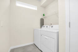 This laundry area features a convenient washer and dryer, complemented by a sleek countertop for folding and organizing. Bright natural light streams in through a small window, enhancing the clean, airy feel of the space.