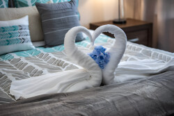 Experience romance with towel swans forming a heart on plush bedding, enhanced by vibrant blue accents and soft gray tones. The inviting textures and elegant decor create a cozy atmosphere ideal for your relaxation.