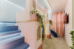 Discover a whimsical play area with a delightful castle design, decorative arches, and lush greenery. The soft pink and blue tones create a playful vibe, and a cozy slide adds extra fun for your little ones.