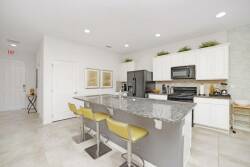 Bright and functional, this kitchen features sleek white cabinetry paired with a striking granite island, perfect for casual dining. The cheerful yellow bar stools add a pop of color, inviting guests to gather and enjoy the space.