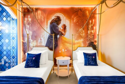 Experience a vibrant room with chic gold-framed beds inviting you to relax. An enchanting wall mural sets a magical tone, and plush blue pillows ensure comfort, making your stay truly delightful.