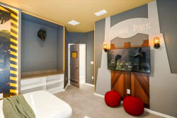 Experience a whimsical bedroom adorned with vibrant Jurassic Park decor, playful wall art, and unique lighting. Cozy red bean bags invite you to relax, while the spacious layout promises a fun and immersive stay for all guests.