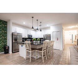 Prepare meals in a bright, fully equipped kitchen with white cabinets, stainless steel appliances, black counters, and pendant lighting. The island with bar seating creates a practical spot for breakfast, snacks, and family time.