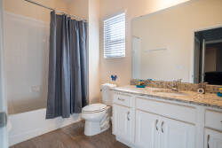 Enjoy a stylish bathroom featuring a sleek granite countertop and a soft gray shower curtain that complements the warm wood-like flooring, creating an inviting atmosphere filled with natural light for your daily routines.
