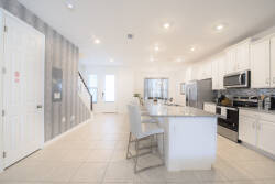 This bright kitchen boasts sleek white cabinetry and a chic gray accent wall, creating an inviting vibe. The spacious island, equipped with modern bar stools, is ideal for casual dining and entertaining with friends.