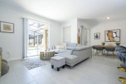 This bright, airy living area is perfect for relaxation, featuring a spacious gray sectional, elegant decor, and a stylish coffee table. Large windows let in natural light, connecting you to the inviting outdoor space.