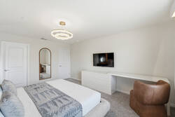 Rest in a bright modern bedroom with a cozy white bed, gray accent throw, warm wood feature wall, soft pendant lights, elegant ceiling fixture, white curtains, and a comfy chair for vacation comfort.