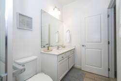 Bright and airy, this bathroom features a spacious vanity with dual sinks and a large mirror that enhances the light, complemented by soft gray tiles. Fresh towels and tasteful decor create a refreshing atmosphere for your stay.