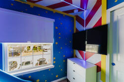 Enjoy a vibrant room with cheerful blue walls and golden stars that uplift your spirit. The sleek white dresser contrasts with a striking red and white striped ceiling, while a large window invites the outdoors in, adding to its.