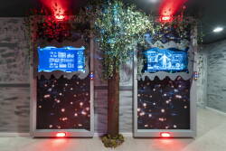 Immerse yourself in a whimsical setting with glowing blue screens and textured walls, featuring a charming faux tree and playful lighting. This unique space invites you to enjoy a fun experience like no other.