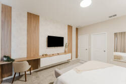 This stylish bedroom combines warm wood accents with a sleek, minimalist design, featuring a contemporary TV setup and a cozy desk area. Soft neutral tones create a serene atmosphere, perfect for your relaxation.