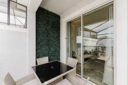 Enjoy your private balcony with a stylish black table perfect for morning coffee or evening cocktails. A lush green wall brings nature close, while large glass doors fill your living area with natural light.