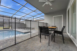 Enjoy outdoor dining in a covered screened patio with a table, black chairs, ceiling fan, sliding glass doors, pool views, and nearby lounge chairs, creating a comfortable space for vacation meals.