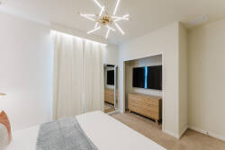 Discover a thoughtfully designed bedroom featuring soft beige tones and natural light that floods the space. The modern chandelier adds an artistic touch, while the subtle textures of the bedding invite relaxation and comfort.