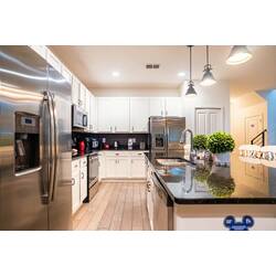 Prepare meals in a bright, fully equipped kitchen with white cabinets, stainless steel appliances, black counters, and pendant lighting. The island with bar seating creates a practical spot for breakfast, snacks, and family time.