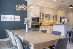 Enjoy culinary delights in this bright kitchen, where a stylish chandelier lights up the warm wood dining table. The soft white cabinetry and intricate tile work create a welcoming atmosphere for shared meals and laughter.