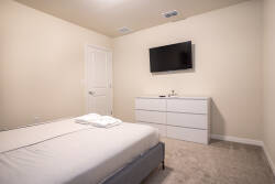 This cozy bedroom offers a soothing neutral palette and plush carpeting for relaxation. Enjoy modern comforts with a sleek dresser, wall-mounted TV, and crisp linens to ensure restful nights after your adventures.