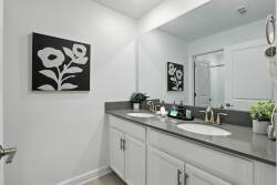 This bright bathroom boasts a sleek double vanity with polished chrome fixtures and a stylish gray countertop, complemented by minimalist decor and black-and-white artwork for a contemporary yet clean aesthetic.