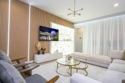 Experience a bright living space with soft, neutral tones and stylish textures. Relax on a cozy sectional sofa while natural light filters through sheer curtains, creating a warm and inviting atmosphere just for you.