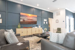 Relax in the cozy ambiance of sunset hues on the striking blue wall, surrounded by plush gray sofas and a sleek wooden coffee table, perfect for enjoying conversations in this stylish living area.
