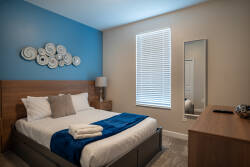 This cozy bedroom boasts a stylish wooden headboard and a calming blue accent wall, creating a soothing atmosphere. Natural light fills the space, enhancing the soft linens and inviting decor for a restful night’s sleep.