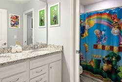 Refresh in a Super Mario themed bathroom with a granite double vanity, large mirror, character wall art, and colorful shower curtain, adding a playful touch to vacation stays.