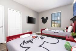 This vibrant bedroom features cheerful red twin beds with Mickey Mouse bedding, ideal for young guests. A flat-screen TV and large windows fill the space with natural light, creating a fun and inviting atmosphere.