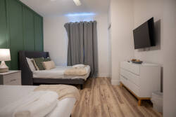 Enjoy restful nights in this stylish room, complete with a cozy dark gray bed, plush linens, and a soothing green accent wall. Natural light streams through elegant curtains, while a sleek TV and modern dresser enhance your stay.