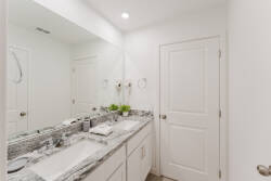 The bright bathroom features a sleek double vanity with a beautiful granite countertop, perfect for your morning routine. Clean white cabinetry complements the modern design, while subtle greenery adds a refreshing touch.