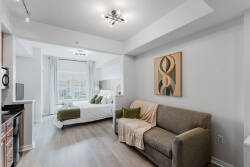 Enjoy the warmth of natural light from large windows illuminating the cozy bed, while modern art enhances the soft gray walls. The plush sofa is perfect for unwinding after a day of adventures and exploring.