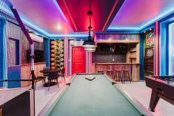 Welcome to our vibrant game room! Challenge your friends at the sleek pool table under lively LED lights, surrounded by sports memorabilia on textured walls, creating an energetic space for both relaxation and fun.