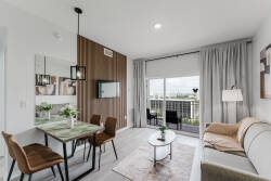 This stylish living space boasts a chic sofa and modern coffee table, enhanced by warm wood accents on the feature wall. Large windows fill the room with natural light, creating a bright atmosphere ideal for relaxation or dining.