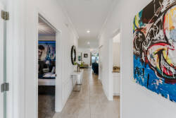 Enter a vibrant hallway filled with striking artwork that contrasts against sleek, light walls. Warm, natural light pours in, creating a welcoming atmosphere that leads you to cozy living spaces just ahead.