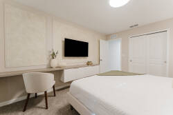 Relax in a cozy bedroom with a plush bed dressed in crisp white linens, a sleek writing desk, and a stylish chair. The soft neutral tones and modern decor create a soothing atmosphere, enhanced by a wall-mounted TV for your.